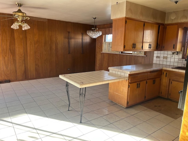 kitchen featuring tile countertops, kitchen peninsula, decorative light fixtures, light tile patterned floors, and ceiling fan with notable chandelier