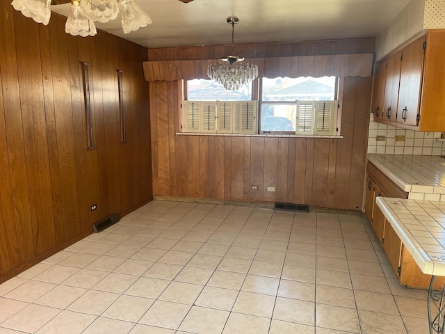 unfurnished dining area featuring light tile patterned floors, an inviting chandelier, and wooden walls