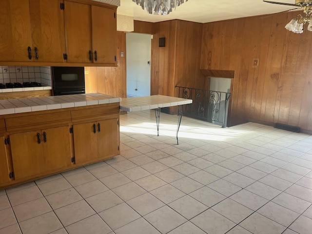 kitchen with tile countertops, ceiling fan, wood walls, and light tile patterned flooring