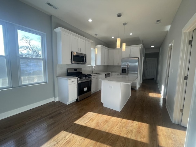 kitchen featuring appliances with stainless steel finishes, sink, white cabinets, a kitchen island, and hanging light fixtures