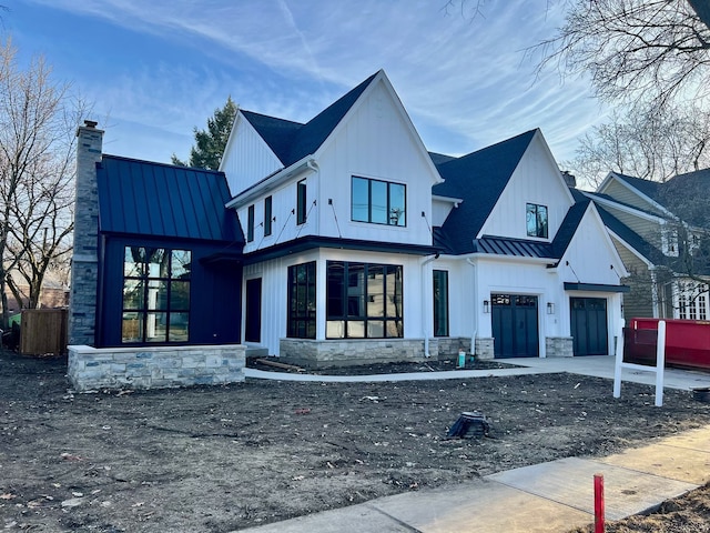 exterior space with a standing seam roof, an attached garage, a chimney, stone siding, and metal roof