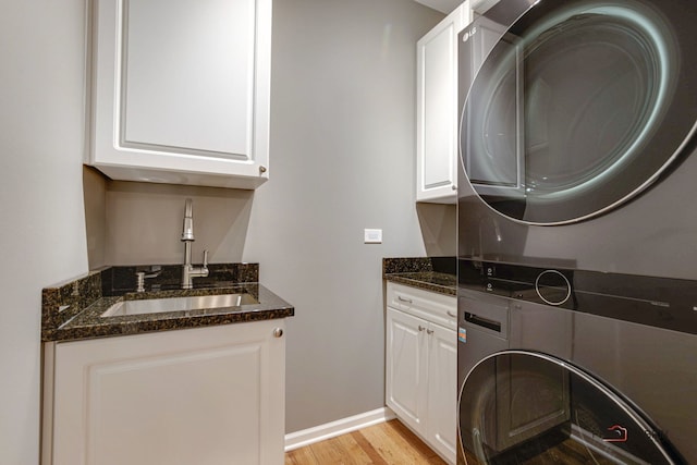 laundry area featuring cabinets, light hardwood / wood-style floors, stacked washer / dryer, and sink