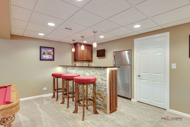 kitchen featuring kitchen peninsula, a paneled ceiling, pendant lighting, stainless steel fridge, and a breakfast bar area