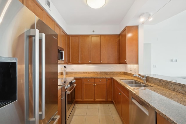 kitchen featuring sink, light tile patterned floors, kitchen peninsula, stainless steel appliances, and light stone countertops