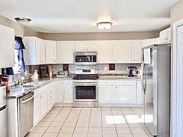 kitchen with appliances with stainless steel finishes, light tile patterned floors, white cabinetry, and sink