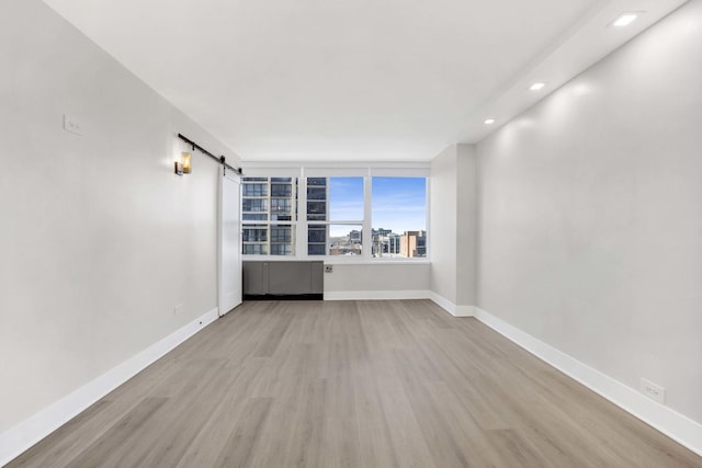 unfurnished room with a barn door and light hardwood / wood-style floors