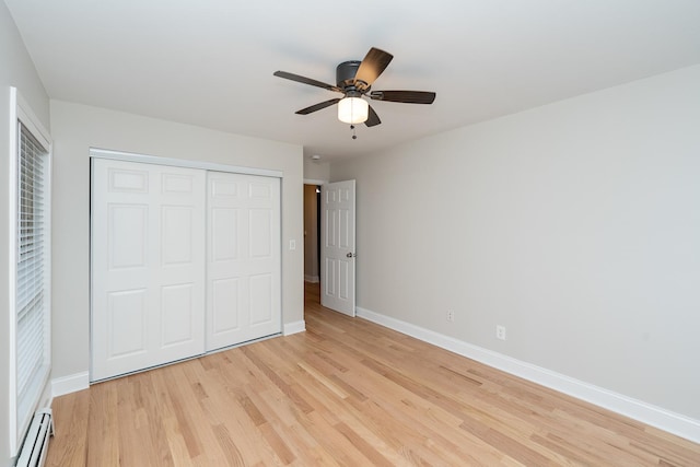 unfurnished bedroom with light wood-type flooring, a closet, ceiling fan, and baseboard heating