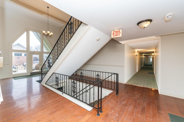 stairway featuring high vaulted ceiling, hardwood / wood-style floors, and an inviting chandelier