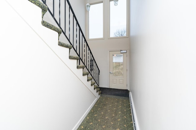 stairway featuring a baseboard heating unit and a high ceiling