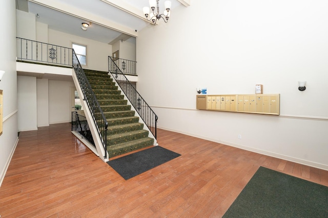 stairs featuring a notable chandelier, a towering ceiling, wood-type flooring, and a mail area