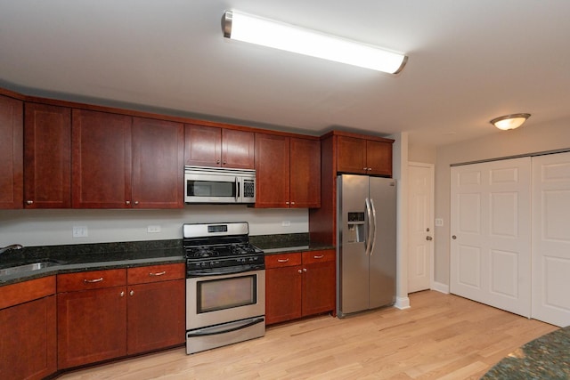 kitchen featuring stainless steel appliances, sink, light hardwood / wood-style floors, and dark stone countertops