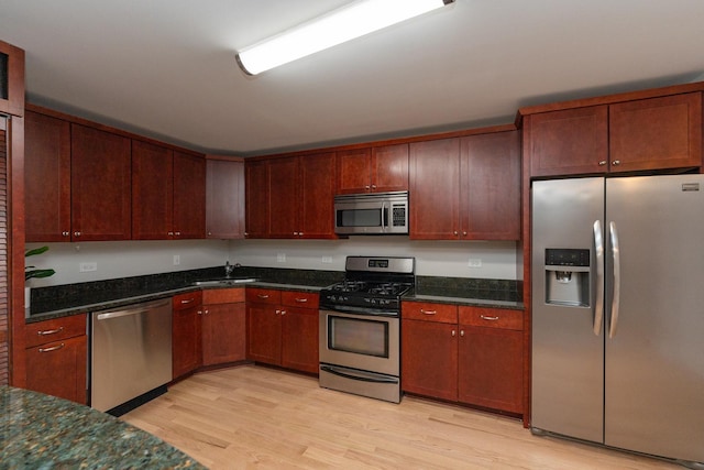 kitchen featuring stainless steel appliances, sink, dark stone countertops, and light wood-type flooring