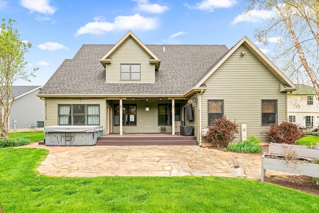 rear view of house with a hot tub, a patio, a shingled roof, and a yard