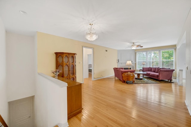 living room featuring ceiling fan with notable chandelier and light hardwood / wood-style flooring