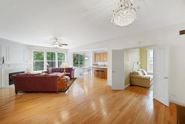 living room featuring ceiling fan with notable chandelier, light hardwood / wood-style flooring, and a tiled fireplace