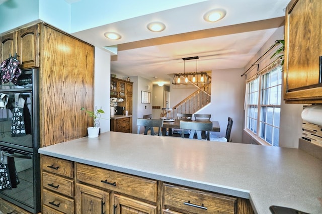 kitchen with kitchen peninsula, black double oven, pendant lighting, and a notable chandelier