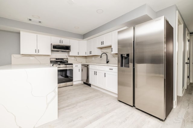 kitchen featuring decorative backsplash, appliances with stainless steel finishes, white cabinetry, and sink