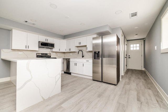 kitchen featuring appliances with stainless steel finishes, light wood-type flooring, tasteful backsplash, light stone counters, and white cabinetry