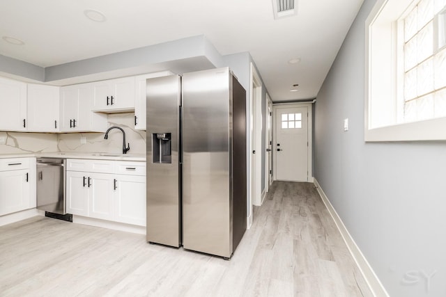 kitchen featuring white cabinetry, sink, stainless steel appliances, light hardwood / wood-style flooring, and decorative backsplash