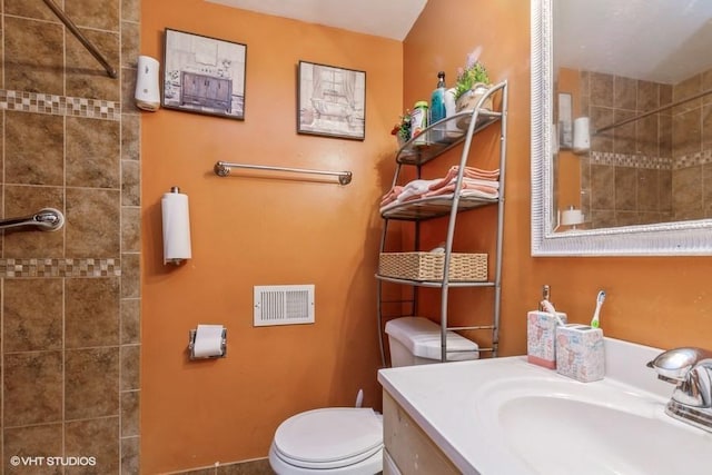 bathroom with toilet, tiled shower, and vanity