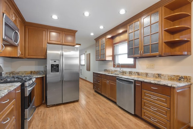 kitchen with appliances with stainless steel finishes, light hardwood / wood-style floors, light stone counters, and sink