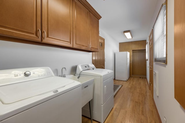 clothes washing area featuring cabinets, light hardwood / wood-style floors, and washer and clothes dryer