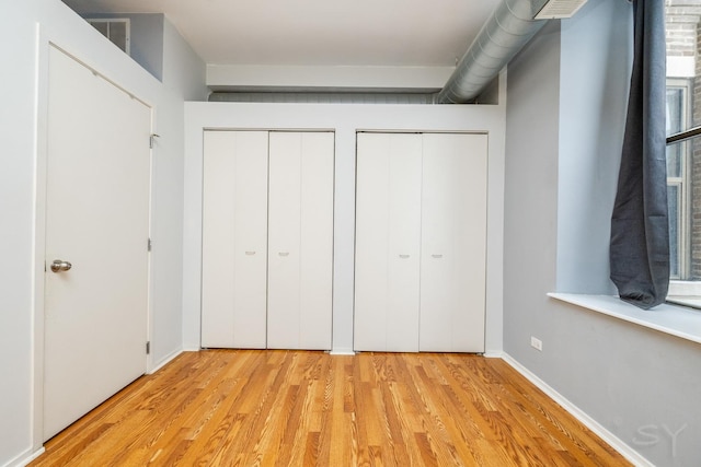 unfurnished bedroom with light hardwood / wood-style flooring and multiple closets