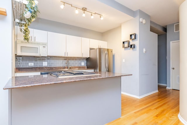 kitchen featuring decorative backsplash, appliances with stainless steel finishes, light wood-type flooring, dark stone countertops, and white cabinetry