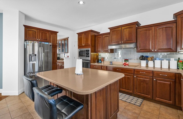 kitchen with light tile patterned floors, a kitchen island, backsplash, stainless steel appliances, and a breakfast bar area