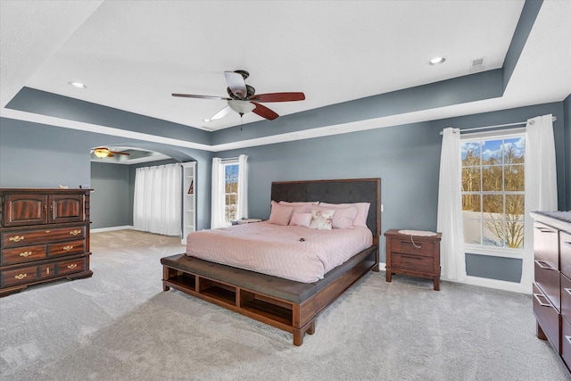 bedroom featuring light carpet, a tray ceiling, and ceiling fan