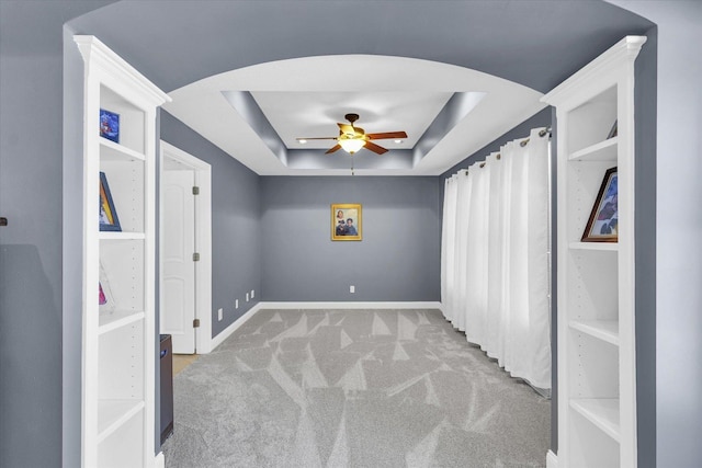 empty room with ceiling fan, light colored carpet, and a tray ceiling