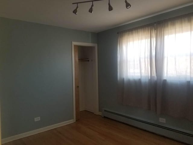 empty room featuring a baseboard radiator, wood-type flooring, and rail lighting