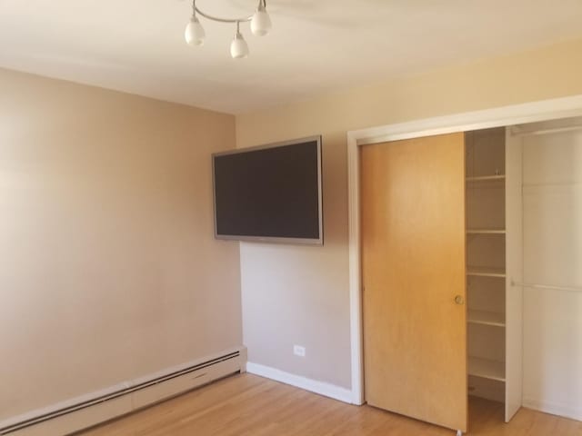 unfurnished bedroom with hardwood / wood-style flooring, a baseboard radiator, and a closet