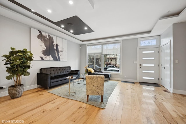 living room with a tray ceiling and light hardwood / wood-style flooring