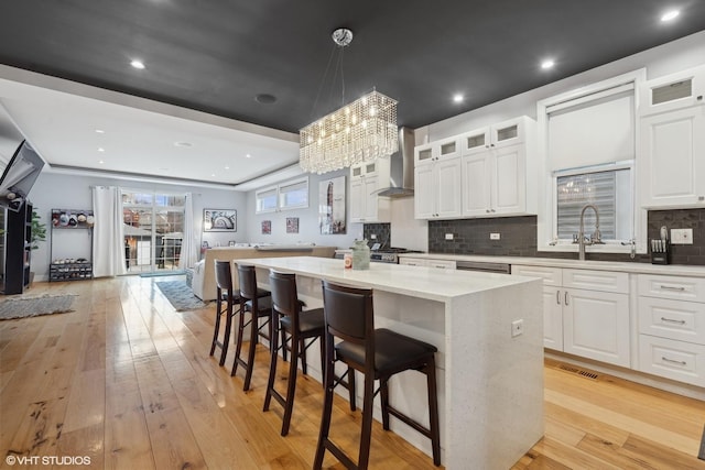 kitchen with white cabinetry, hanging light fixtures, a center island, wall chimney range hood, and light hardwood / wood-style flooring