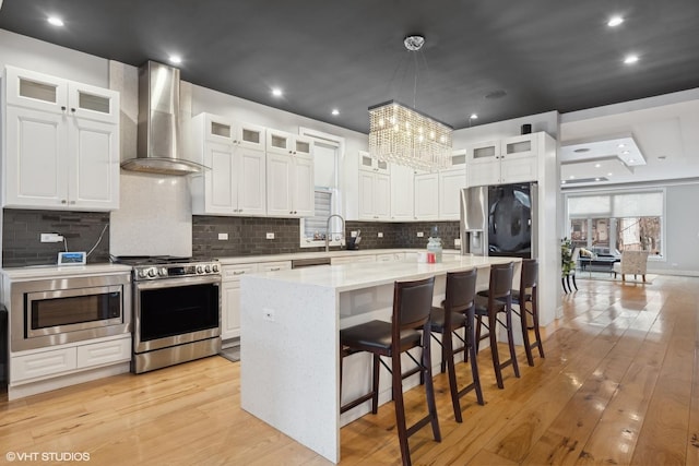 kitchen featuring wall chimney range hood, light hardwood / wood-style flooring, stainless steel appliances, a center island, and white cabinets