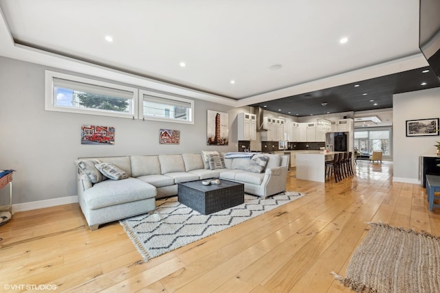 living room featuring light hardwood / wood-style floors, a raised ceiling, and a healthy amount of sunlight