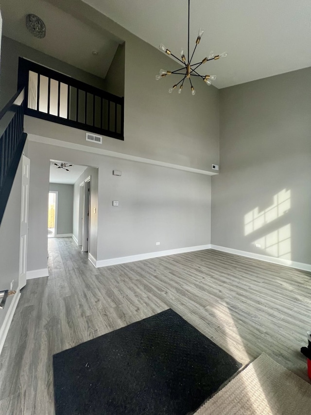 unfurnished living room with wood-type flooring, a high ceiling, and an inviting chandelier