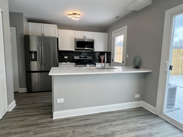 kitchen with tasteful backsplash, kitchen peninsula, white cabinets, and stainless steel appliances