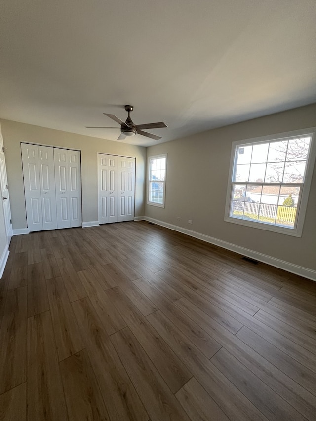 unfurnished bedroom with two closets, ceiling fan, and dark hardwood / wood-style floors