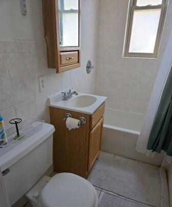 bathroom with tile patterned floors, tile walls, toilet, and a healthy amount of sunlight