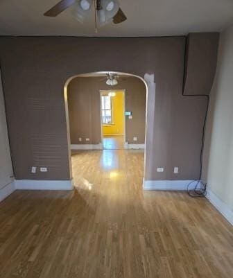 unfurnished room featuring baseboards, arched walkways, wood finished floors, and a ceiling fan