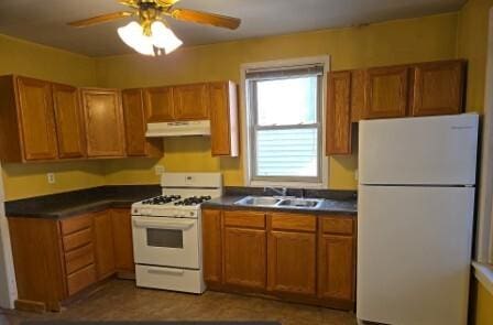 kitchen featuring a sink, under cabinet range hood, dark countertops, white appliances, and brown cabinetry