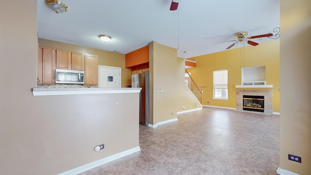 kitchen with a tile fireplace, ceiling fan, appliances with stainless steel finishes, decorative backsplash, and kitchen peninsula