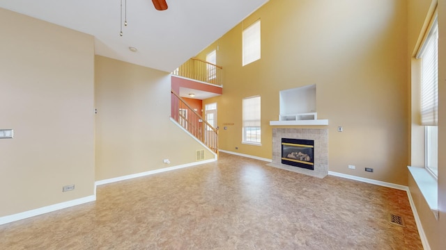 unfurnished living room featuring a tiled fireplace, a towering ceiling, and ceiling fan