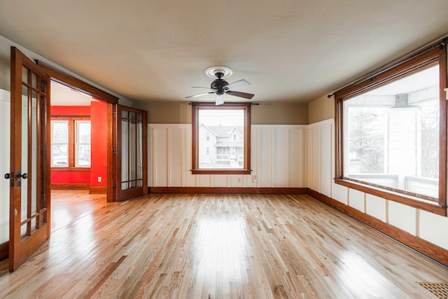 spare room with a wealth of natural light, french doors, ceiling fan, and light wood-type flooring