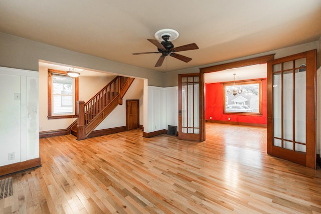 spare room featuring ceiling fan with notable chandelier, light wood-type flooring, and french doors