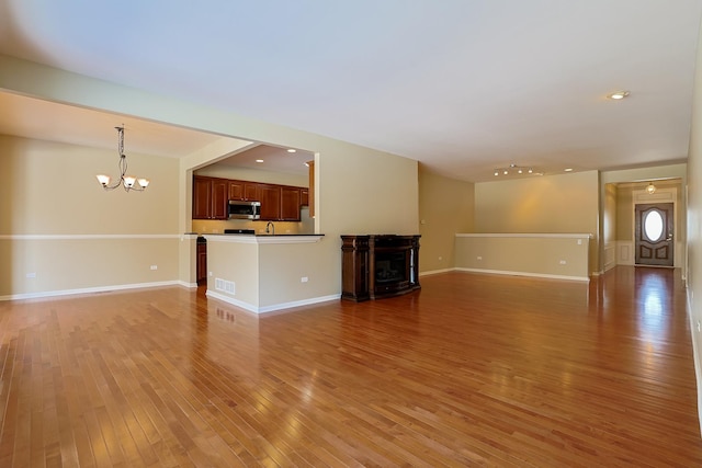 unfurnished living room featuring wood-type flooring, sink, and a notable chandelier