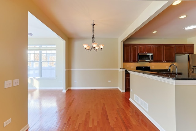 kitchen with pendant lighting, appliances with stainless steel finishes, a notable chandelier, dark stone counters, and light wood-type flooring