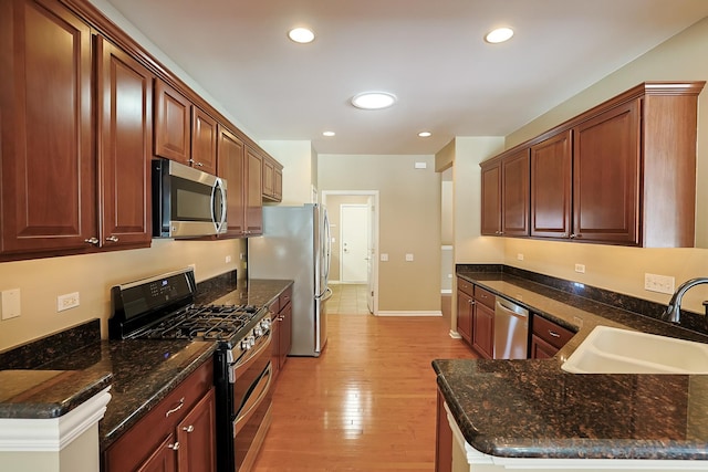 kitchen featuring sink, light hardwood / wood-style flooring, dark stone countertops, stainless steel appliances, and kitchen peninsula